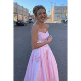 Vestido largo de fiesta rosa satinado de corte evasé con tirantes finos, escote redondo y bolsillos.