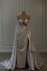 Magnifique robe de mariée longue blanche en satin, sans manches, ornée de perles et fendue.