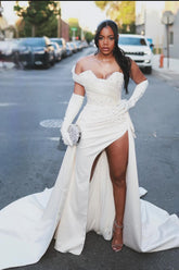 Precioso vestido de novia blanco de corte columna, de satén, sin mangas, con un solo hombro y cola con abertura y detalles de pedrería.