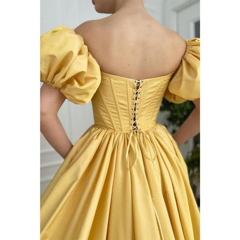 Vestido largo de fiesta amarillo satinado sin tirantes, de manga corta, con abertura alta y bolsillos. 