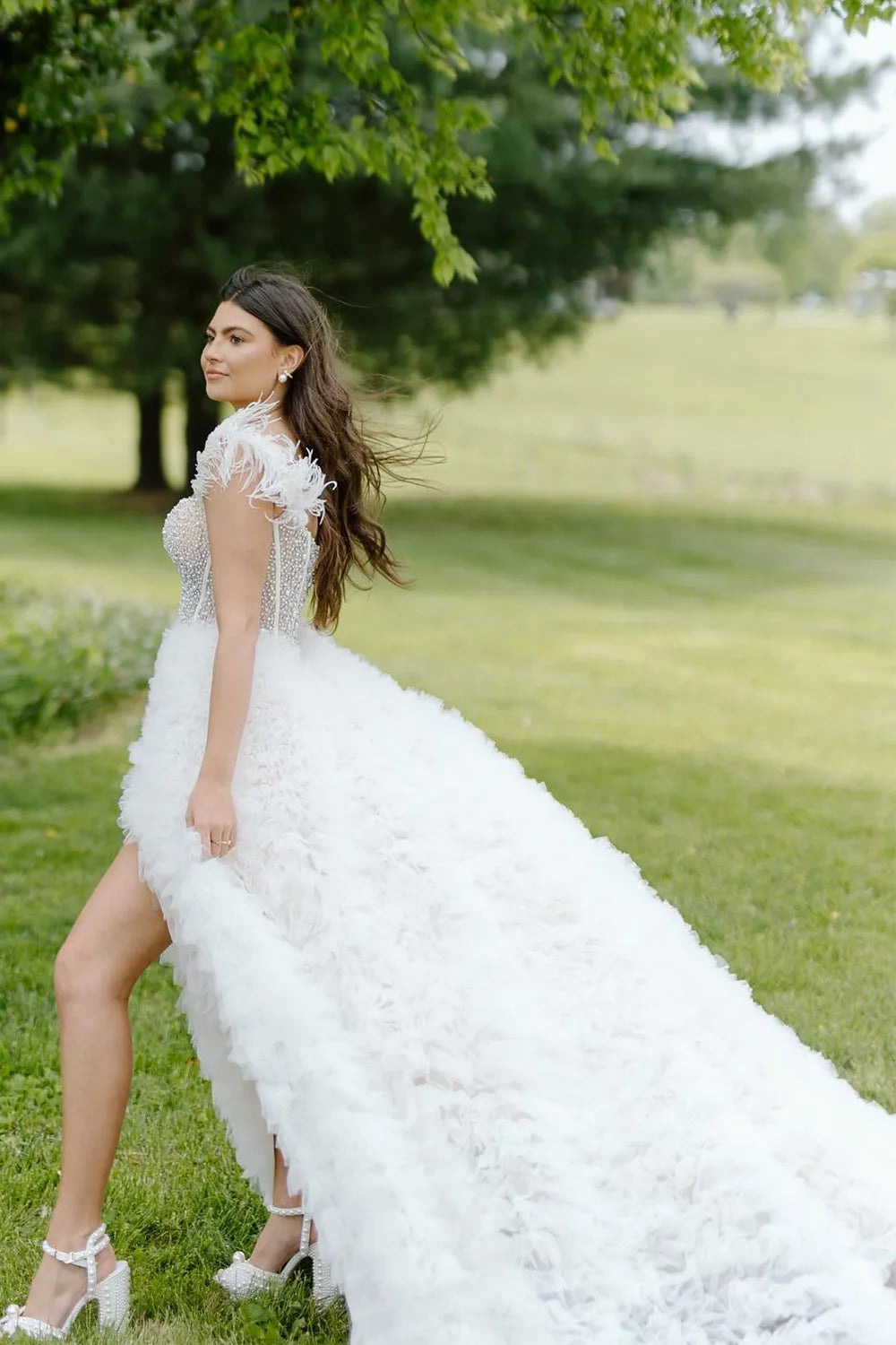 Robe de bal longue bustier trapèze en tulle à épaules dénudées et à volants, ornée de plumes.