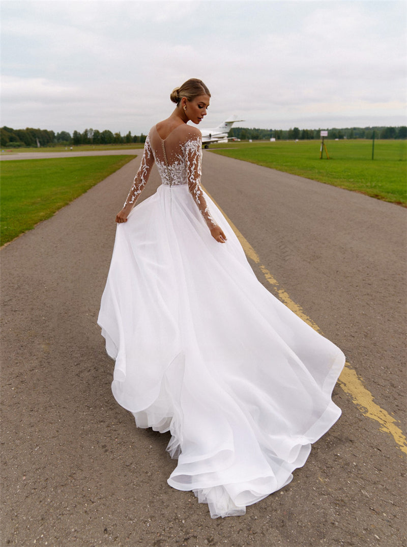 Robe de mariée blanche en organza et tulle, coupe trapèze, ornée de cristaux et à manches longues, avec col transparent. 