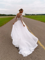 Robe de mariée blanche en organza et tulle, coupe trapèze, ornée de cristaux et à manches longues, avec col transparent. 