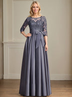 Robe de mariée longue en satin et dentelle, coupe trapèze, décolleté illusion, ornée d'un nœud à sequins. 