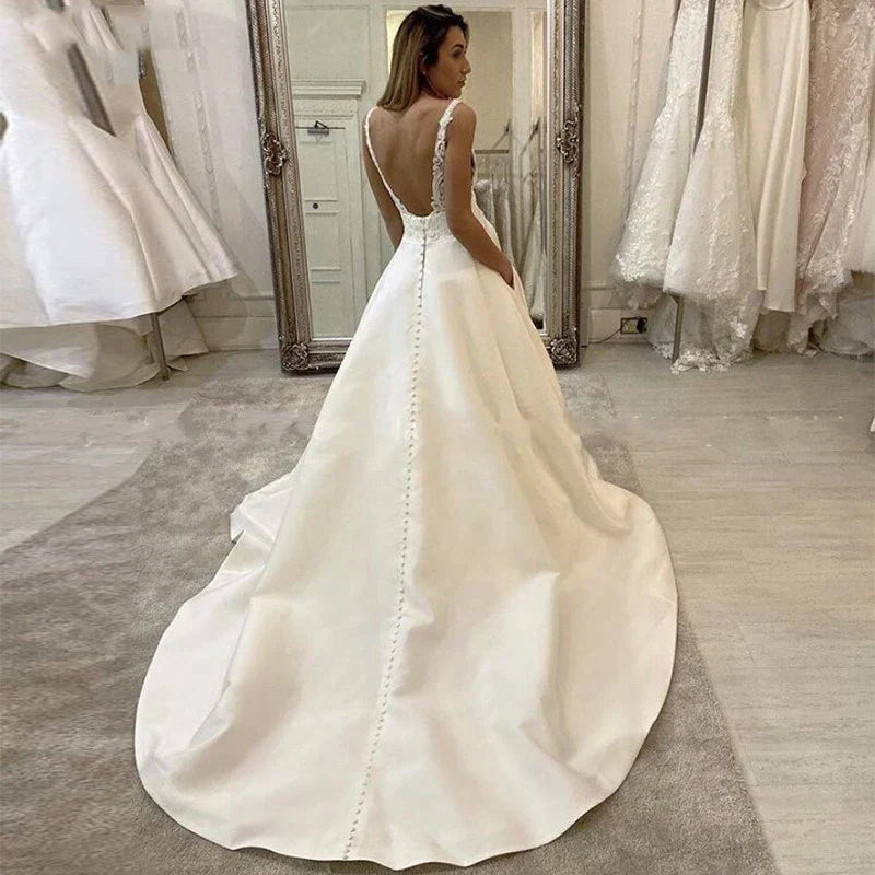Vestido de novia blanco satinado corte A, escote en V profundo, estilo boho, con apliques sencillos, espalda descubierta y bolsillo.