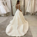 Vestido de novia blanco satinado corte A, escote en V profundo, estilo boho, con apliques sencillos, espalda descubierta y bolsillo.