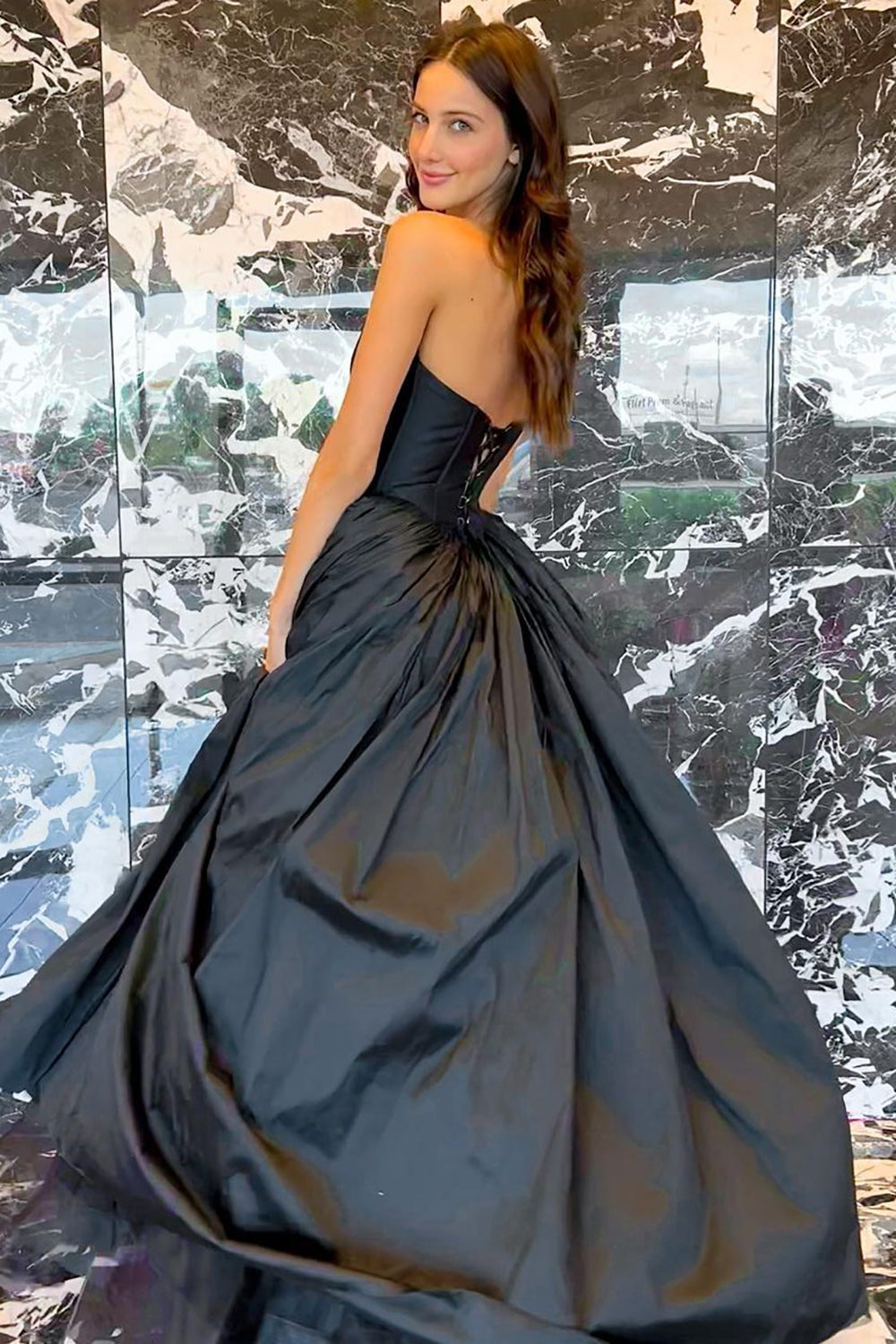 Vestido de fiesta negro de corte A, sin tirantes y con corsé, con espalda cruzada.