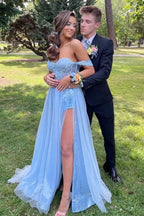 Vestido largo de fiesta azul con escote barco, hombros descubiertos, apliques y abertura frontal.