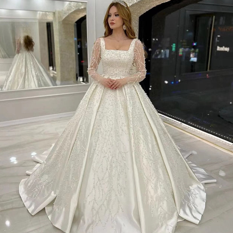 Vestido de novia de lujo con encaje bordado y pedrería, corte princesa, cuello cuadrado, manga larga y botones. 