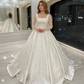 Vestido de novia de lujo con encaje bordado y pedrería, corte princesa, cuello cuadrado, manga larga y botones. 
