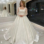 Vestido de novia de lujo con encaje bordado y pedrería, corte princesa, cuello cuadrado, manga larga y botones. 