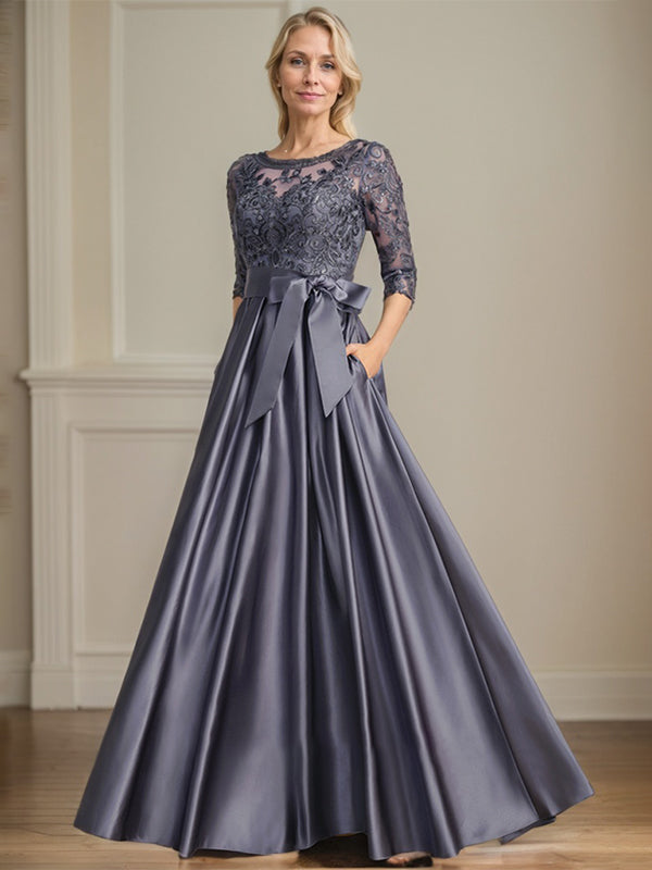 Robe de mariée longue en satin et dentelle, coupe trapèze, décolleté illusion, ornée d'un nœud à sequins. 