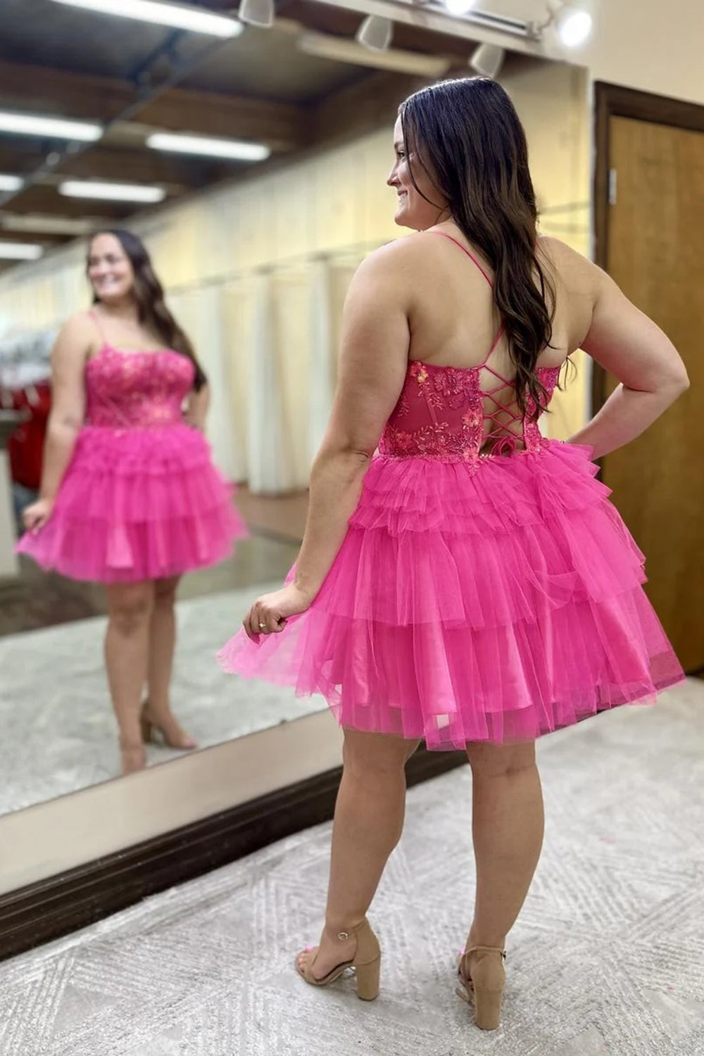 Vestido corto de fiesta de bienvenida con tirantes finos, corte en A, tul escalonado, corsé y apliques en color rosa fucsia.
