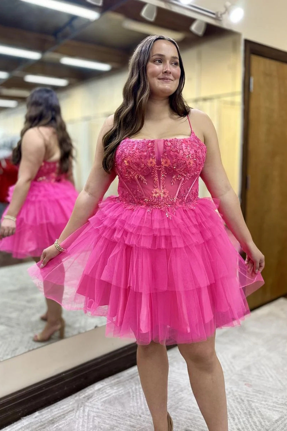 Vestido corto de fiesta de bienvenida con tirantes finos, corte en A, tul escalonado, corsé y apliques en color rosa fucsia.