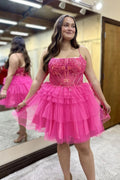 Vestido corto de fiesta de bienvenida con tirantes finos, corte en A, tul escalonado, corsé y apliques en color rosa fucsia.