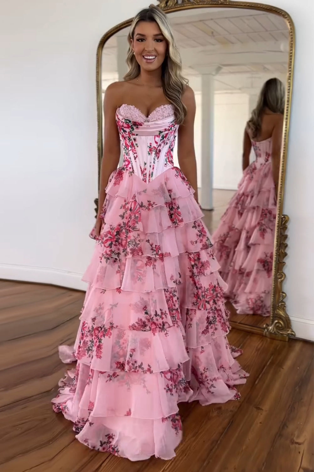 Robe de bal longue bustier à volants en mousseline de soie rose poudré, coupe trapèze, ornée de fleurs et fendue.