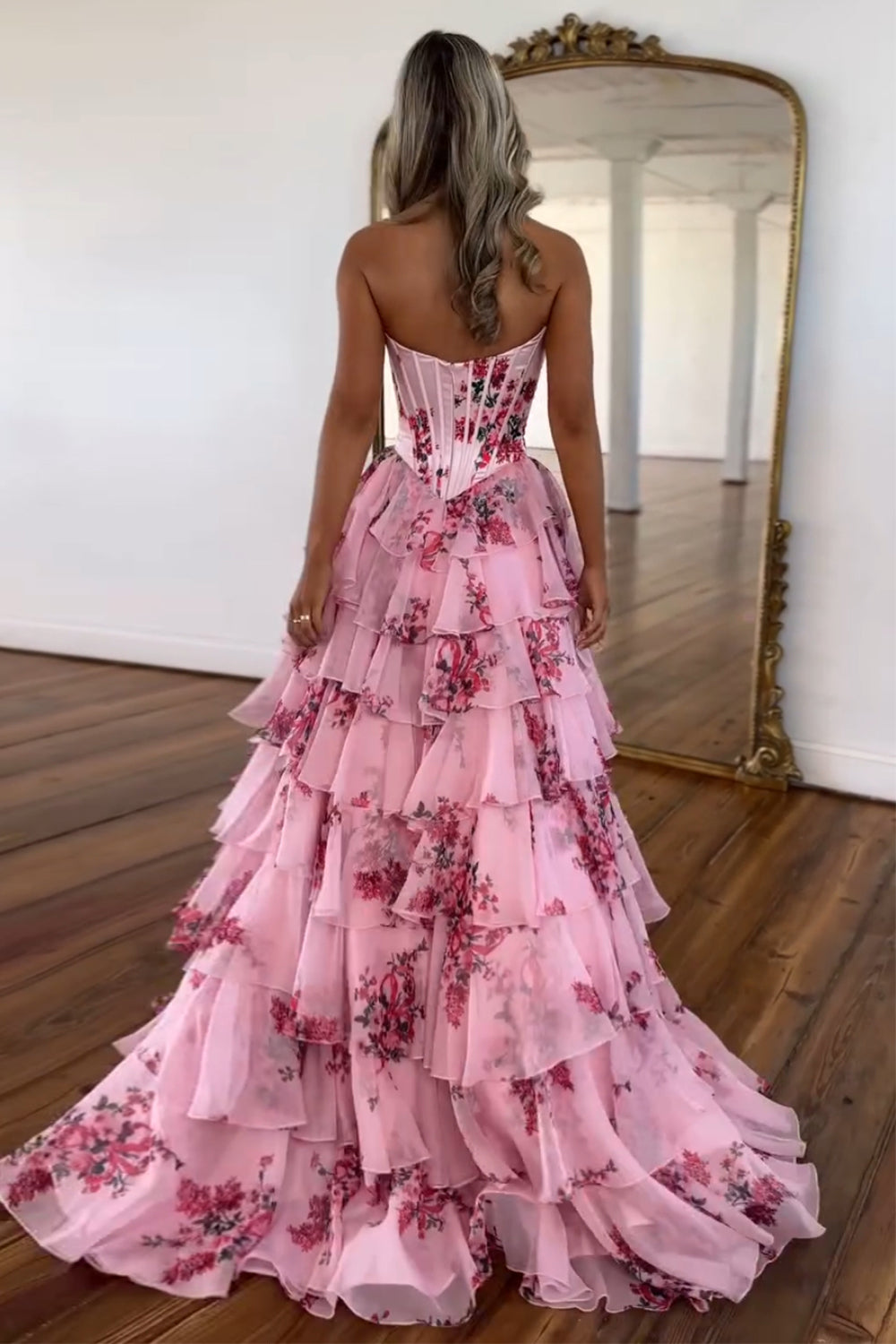 Robe de bal longue bustier à volants en mousseline de soie rose poudré, coupe trapèze, ornée de fleurs et fendue.