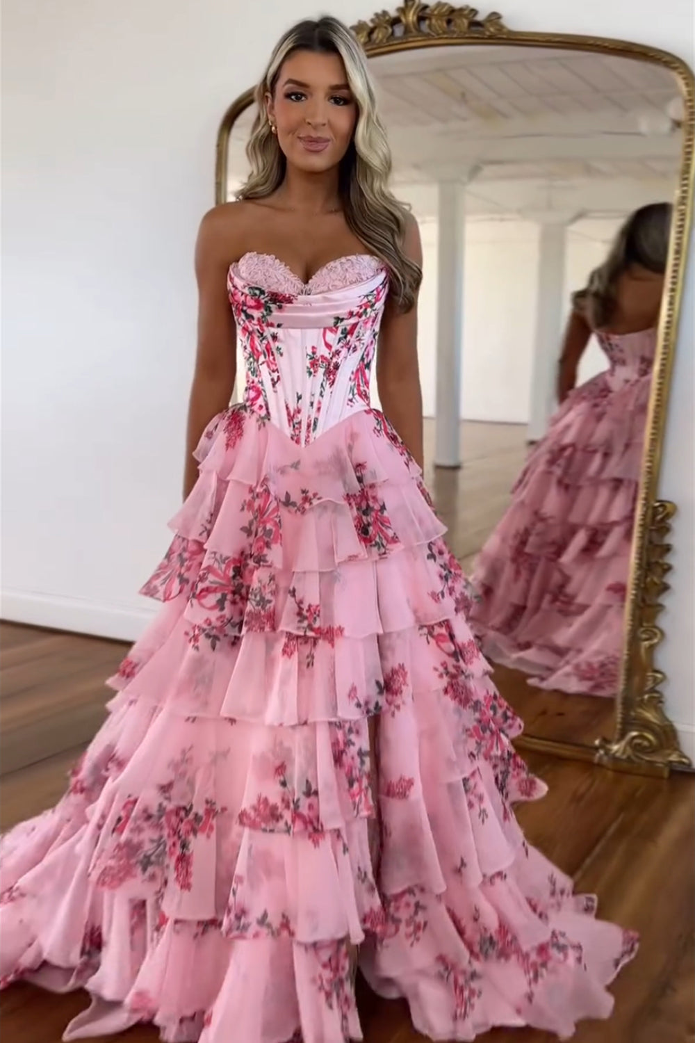 Robe de bal longue bustier à volants en mousseline de soie rose poudré, coupe trapèze, ornée de fleurs et fendue.