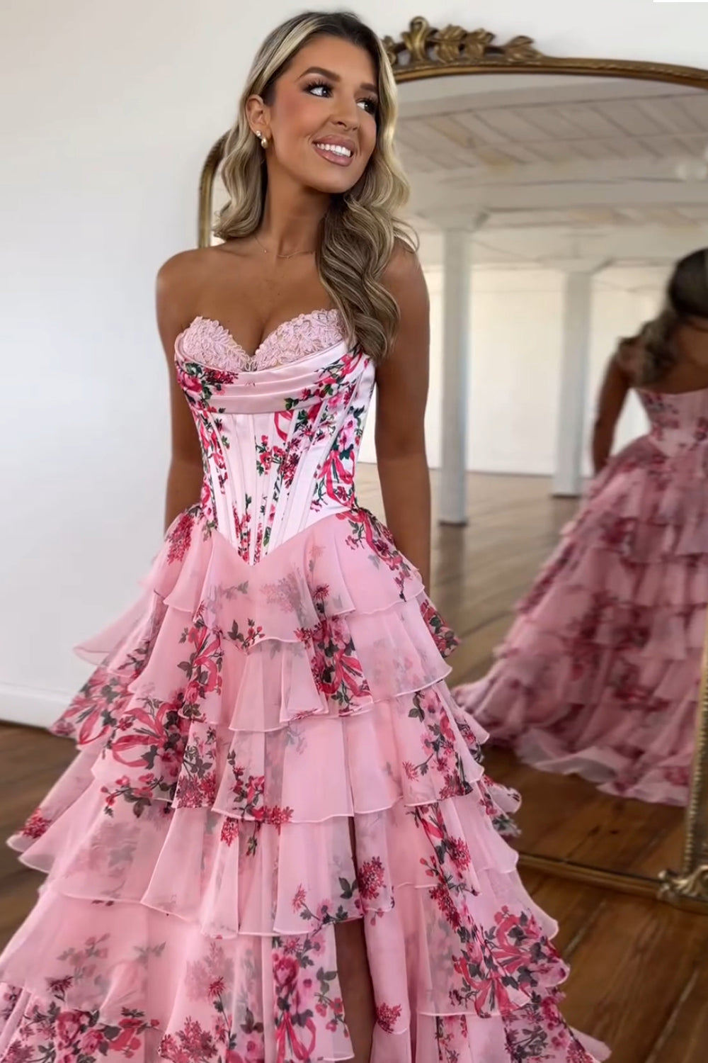 Robe de bal longue bustier à volants en mousseline de soie rose poudré, coupe trapèze, ornée de fleurs et fendue.