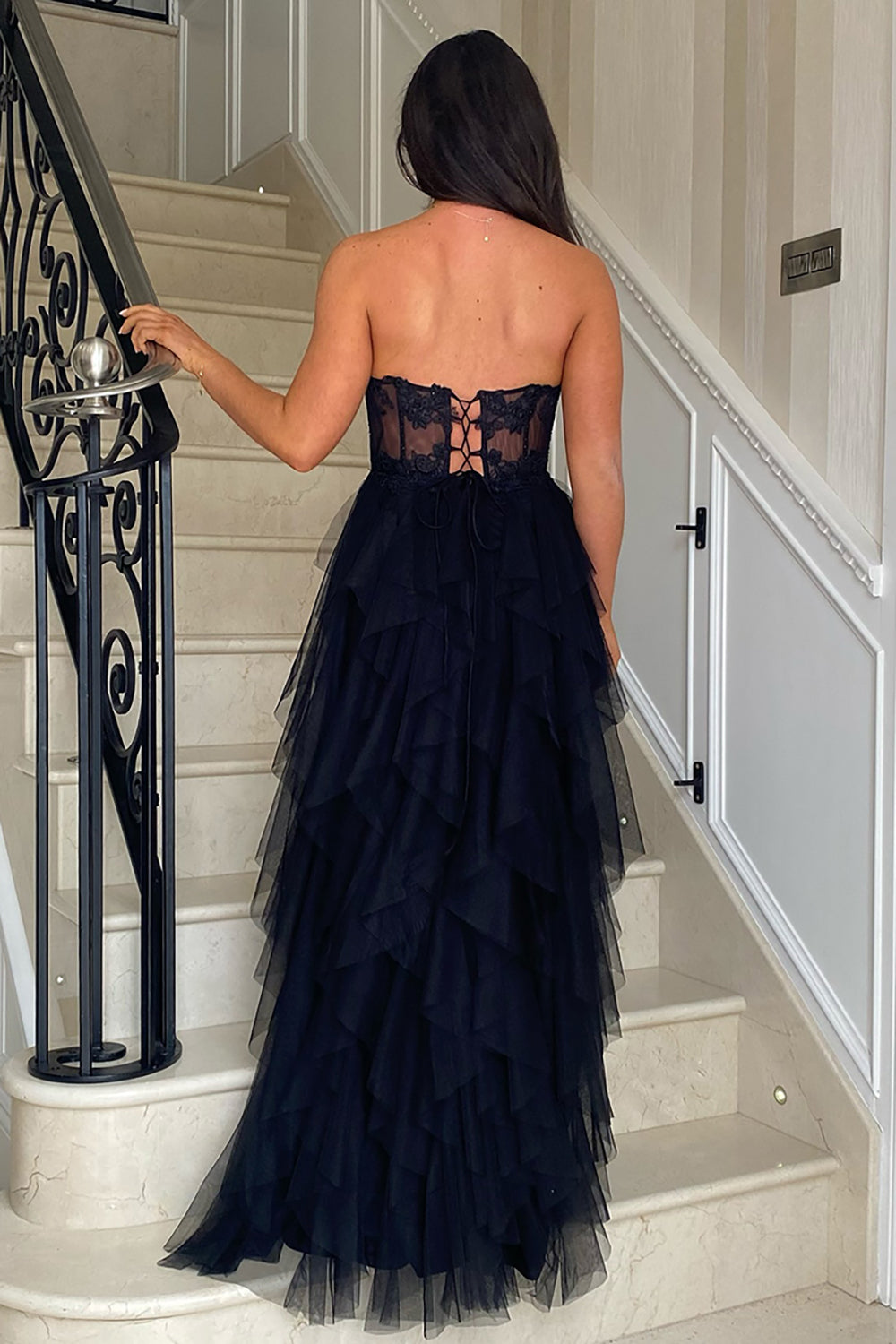 Robe de bal longue bustier en tulle rose poudré, coupe trapèze, à volants et corset orné d'appliques