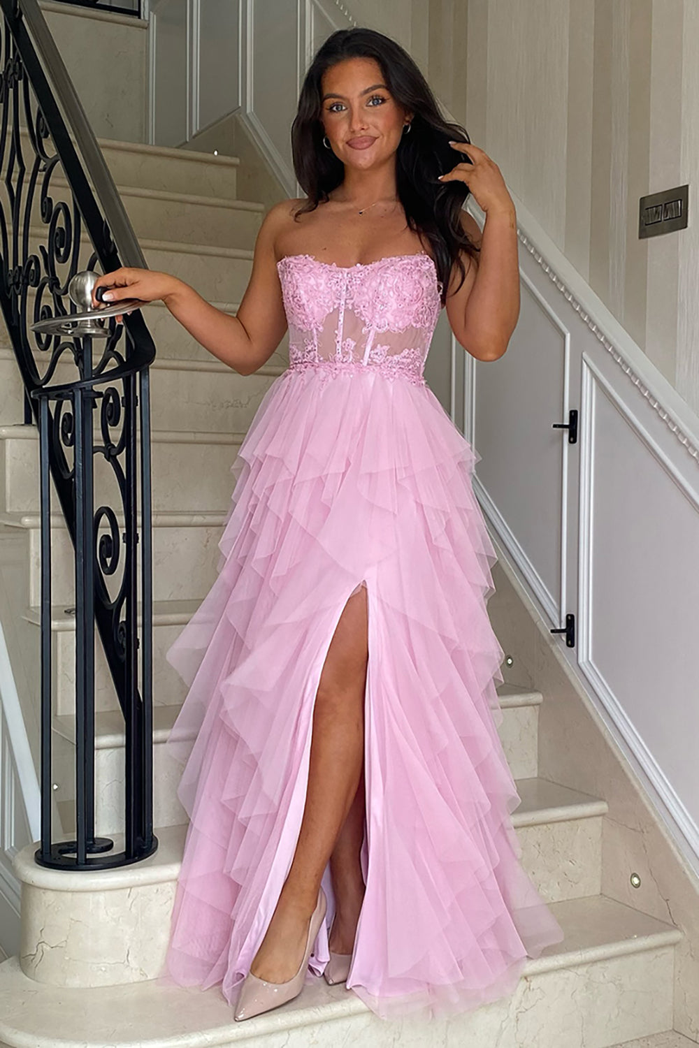 Robe de bal longue bustier en tulle rose poudré, coupe trapèze, à volants et corset orné d'appliques