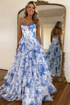 Robe de bal longue bustier à volants en mousseline de soie rose poudré, coupe trapèze, ornée de fleurs et fendue.