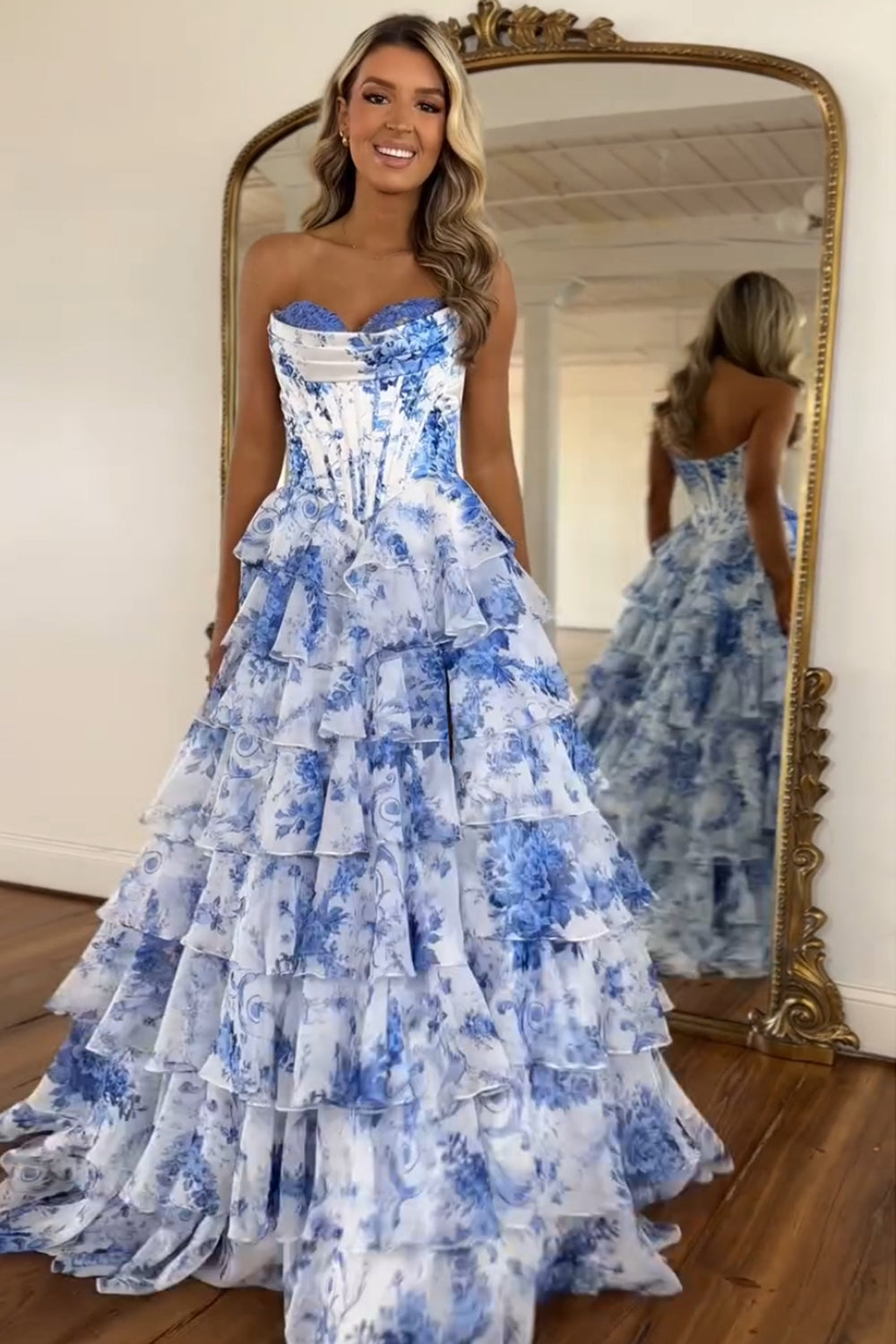 Robe de bal longue bustier à volants en mousseline de soie rose poudré, coupe trapèze, ornée de fleurs et fendue.