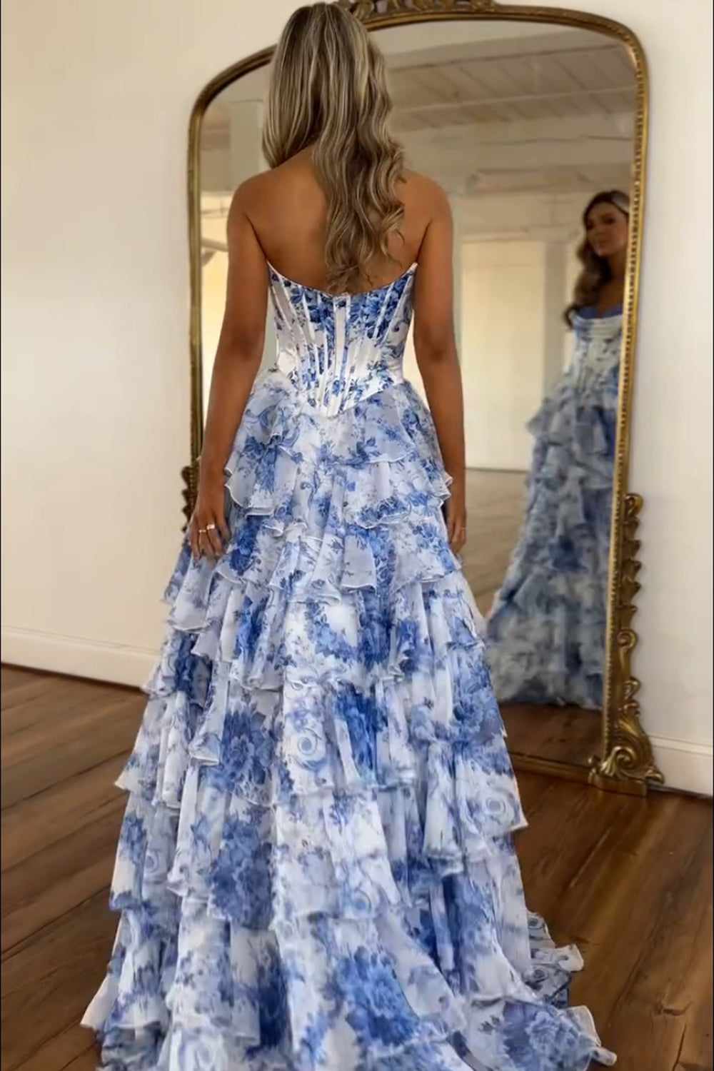 Robe de bal longue bustier à volants en mousseline de soie rose poudré, coupe trapèze, ornée de fleurs et fendue.