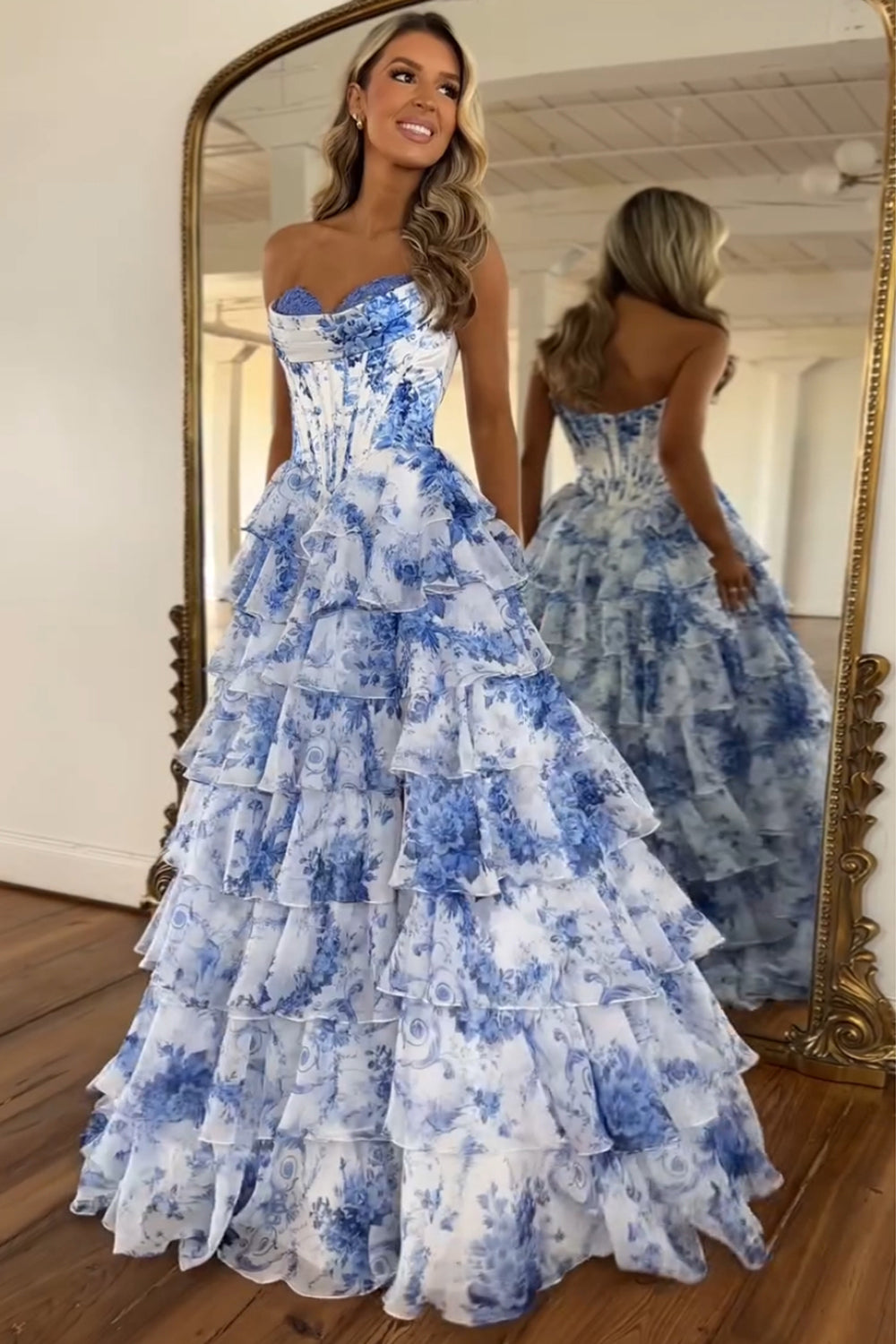 Robe de bal longue bustier à volants en mousseline de soie rose poudré, coupe trapèze, ornée de fleurs et fendue.