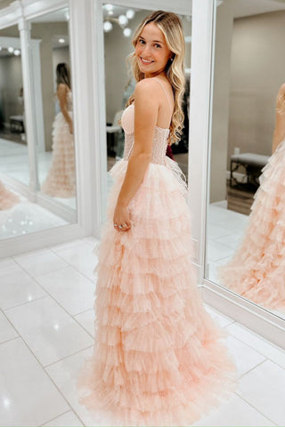 Robe de bal longue trapèze en tulle rose poudré à fines bretelles et à volants, ornée de perles.