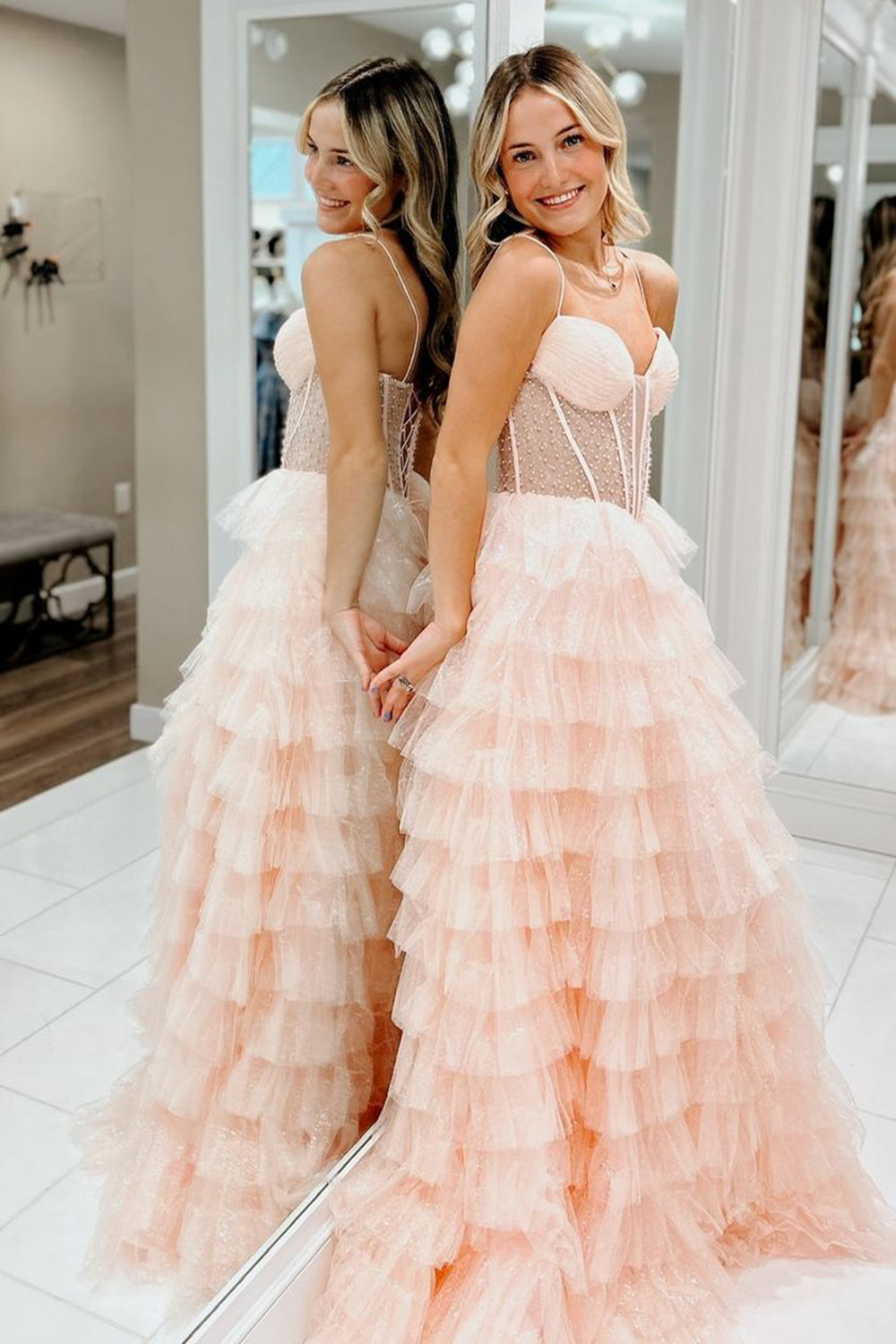 Robe de bal longue trapèze en tulle rose poudré à fines bretelles et à volants, ornée de perles.