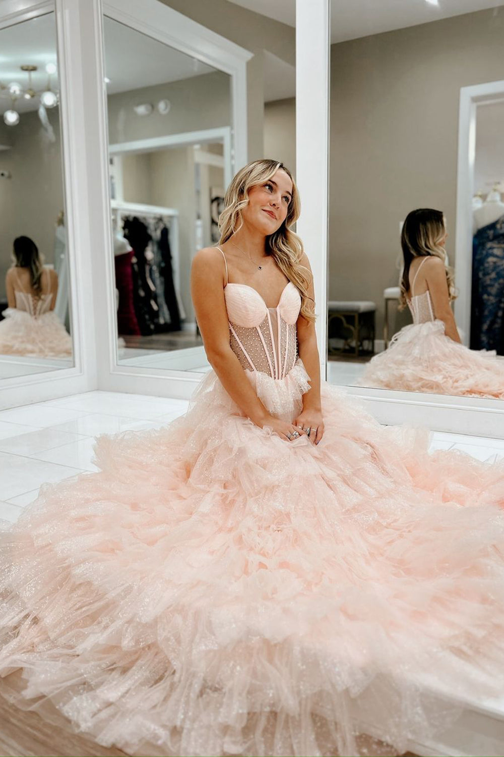 Robe de bal longue trapèze en tulle rose poudré à fines bretelles et à volants, ornée de perles.