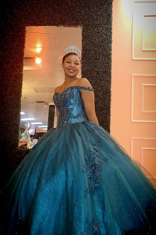 Vestido de quinceañera azul pavo real con hombros descubiertos, estilo princesa, con apliques y pedrería.