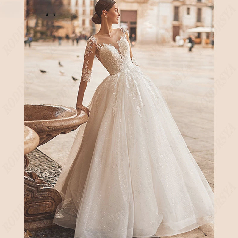 Vestido de novia con escote redondo, espalda ilusión, corte en A, tul, manga 3/4, apliques de encaje. 