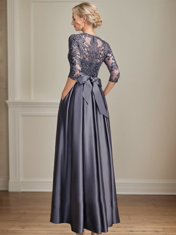 Robe de mariée longue en satin et dentelle, coupe trapèze, décolleté illusion, ornée d'un nœud à sequins. 