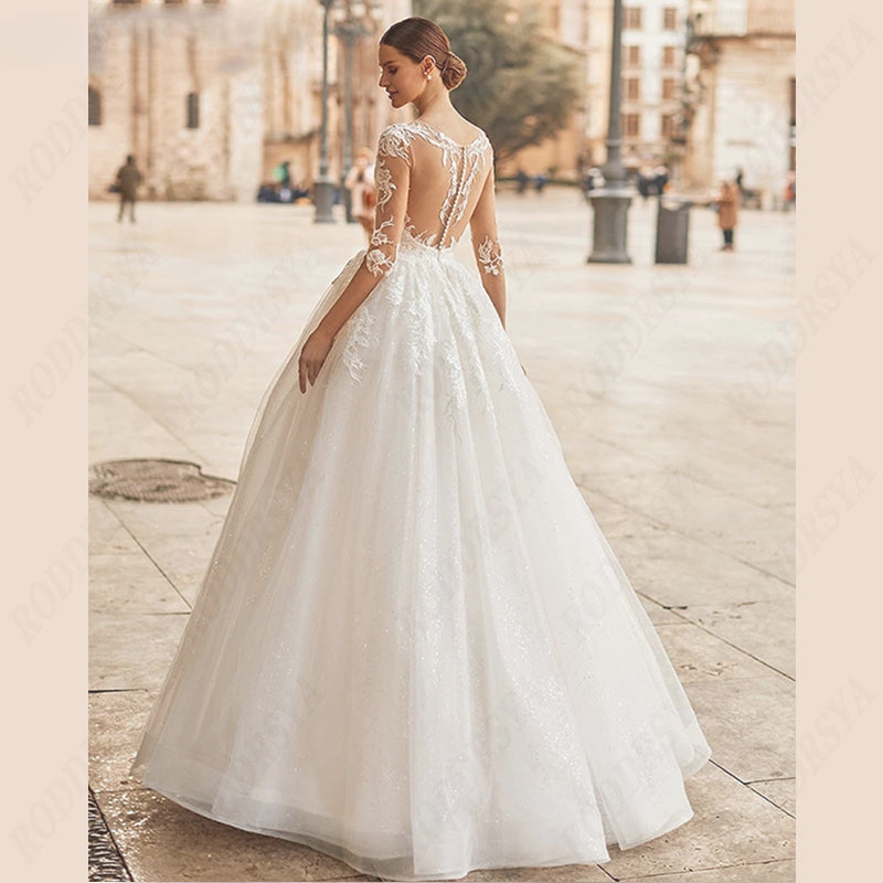 Vestido de novia con escote redondo, espalda ilusión, corte en A, tul, manga 3/4, apliques de encaje. 