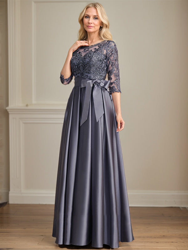 Robe de mariée longue en satin et dentelle, coupe trapèze, décolleté illusion, ornée d'un nœud à sequins. 