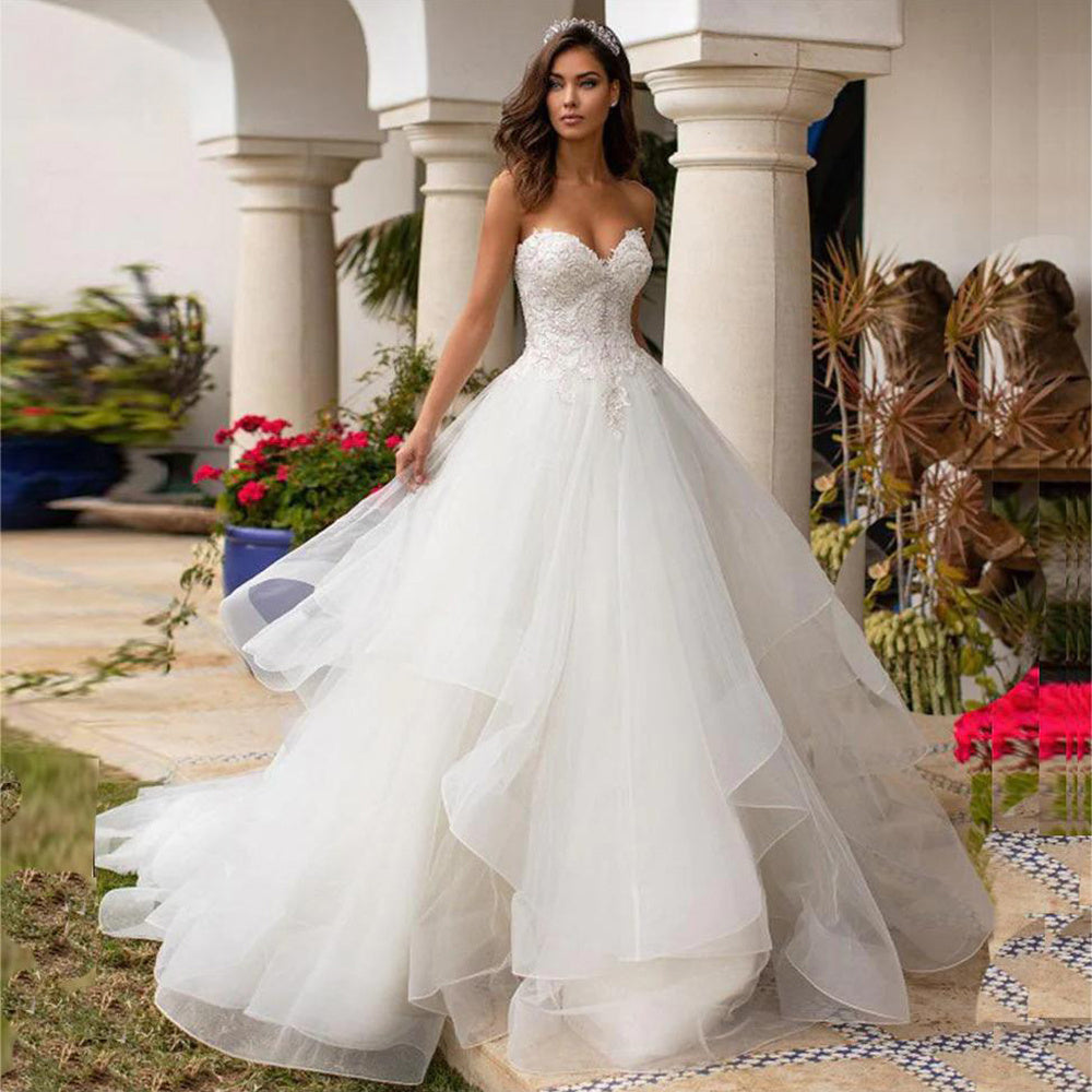 Vestido de novia de lujo estilo princesa, con espalda descubierta, corpiño de lentejuelas y pedrería, escote corazón, apliques de encaje y falda de organza con volumen. 