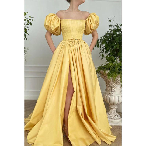 Vestido largo de fiesta amarillo satinado sin tirantes, de manga corta, con abertura alta y bolsillos. 