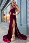 Robe de soirée longue asymétrique en velours bordeaux ornée de perles et fendue.