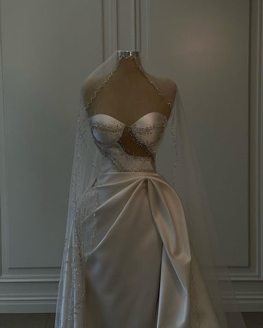 Magnifique robe de mariée longue blanche en satin, sans manches, ornée de perles et fendue.