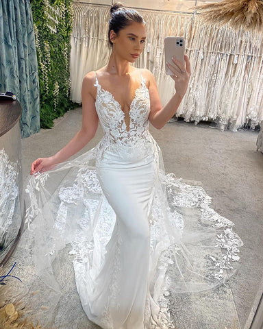 Magnifique robe de mariée sirène blanche longue sans manches à col V et fines bretelles spaghetti, ornée de dentelle.
