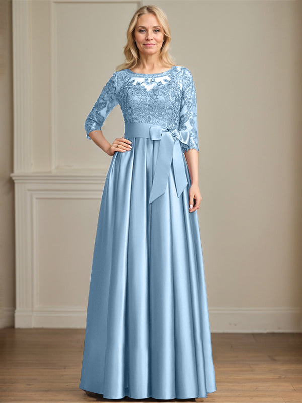 Robe de mariée longue en satin et dentelle, coupe trapèze, décolleté illusion, ornée d'un nœud à sequins. 