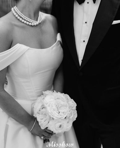 Precioso vestido de novia blanco de corte A, con hombros descubiertos, escote redondo, sin mangas, volantes y abertura frontal en satén.