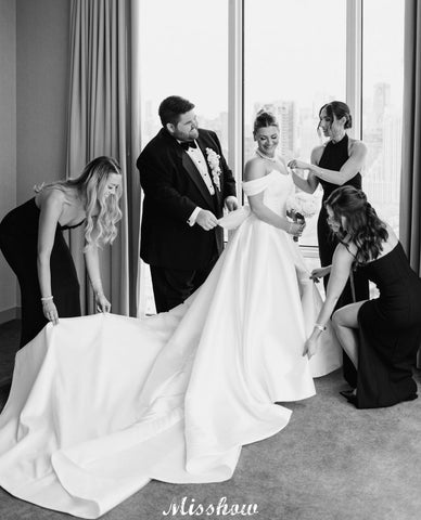 Precioso vestido de novia blanco de corte A, con hombros descubiertos, escote redondo, sin mangas, volantes y abertura frontal en satén.