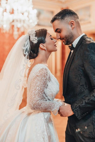 Robe de mariée longue trapèze en dentelle ornée de sequins et de perles, manches longues et traîne amovible.