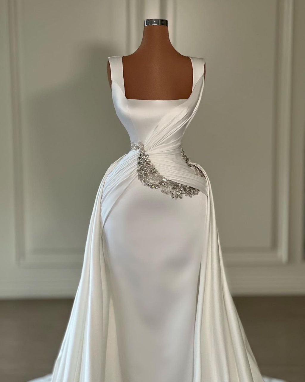 Vestido de novia largo de corte A, color marfil, con tirantes, joyas, sin mangas y cola.