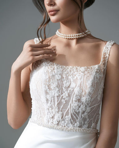 Robe de mariée blanche élégante, longue, trapèze, ornée de perles et de dentelle, sans manches et fendue.