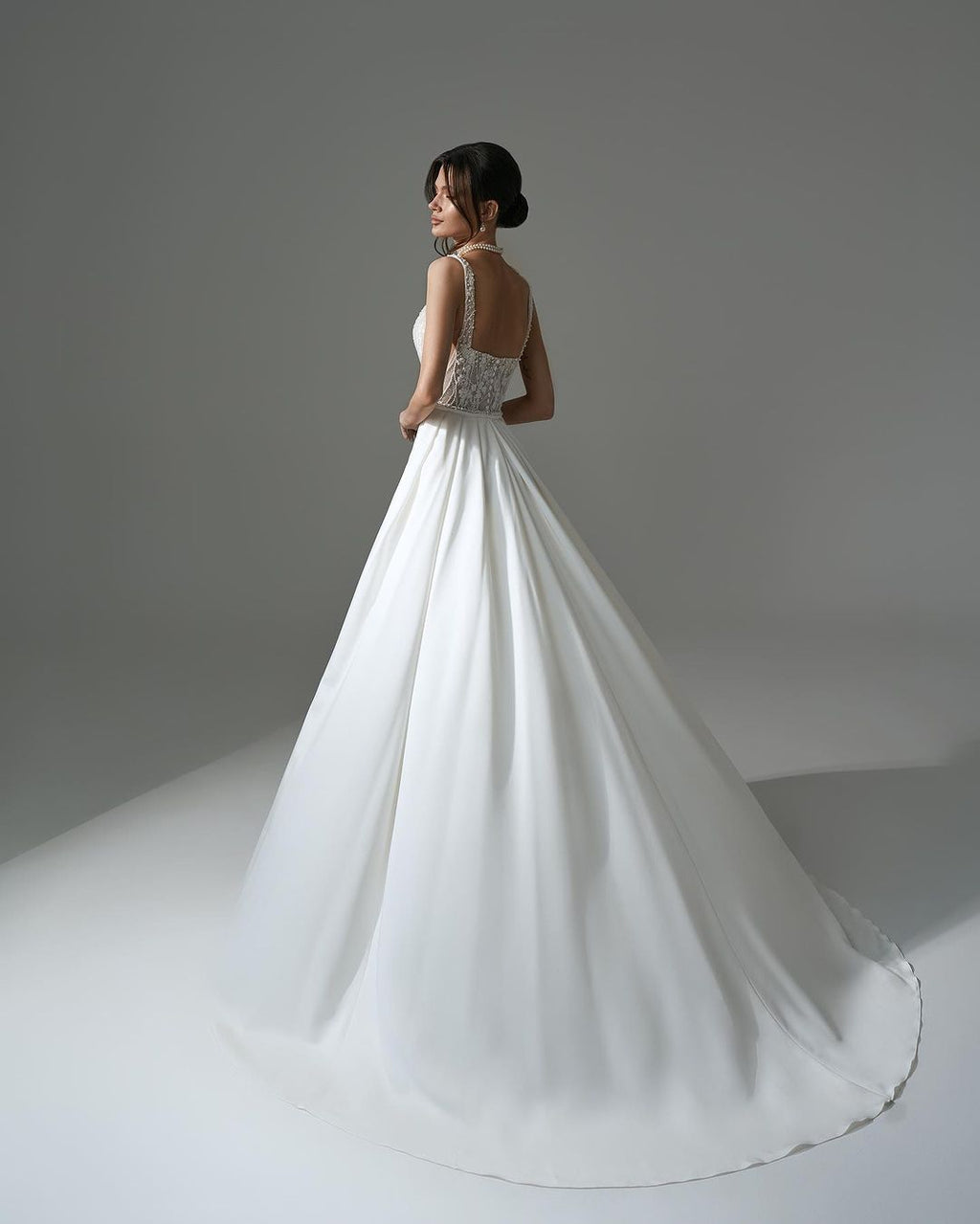 Robe de mariée blanche élégante, longue, trapèze, ornée de perles et de dentelle, sans manches et fendue.