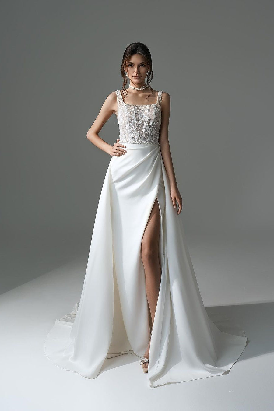 Robe de mariée blanche élégante, longue, trapèze, ornée de perles et de dentelle, sans manches et fendue.